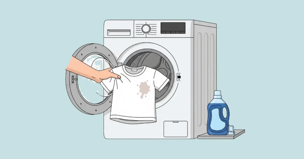 A hand placing a stained white t-shirt into an open washing machine, with a bottle of liquid laundry detergent nearby.
